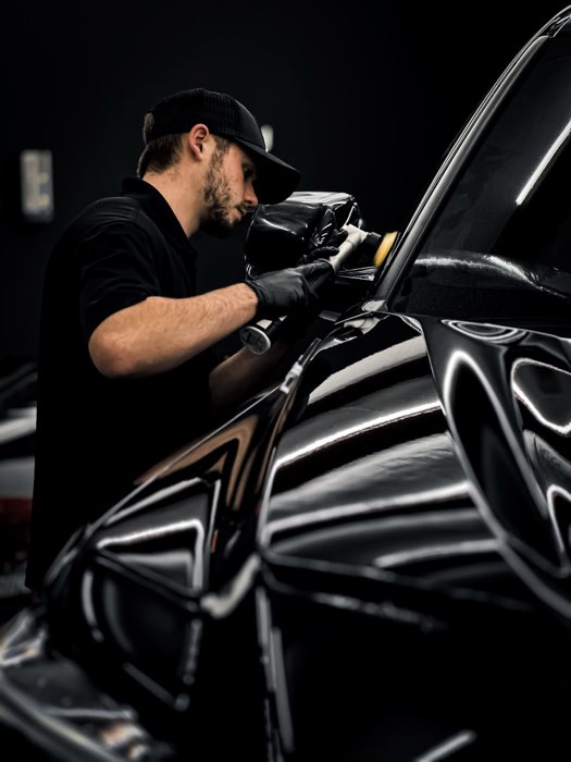 Técnico a polir a pintura de um carro preto com polidora orbital